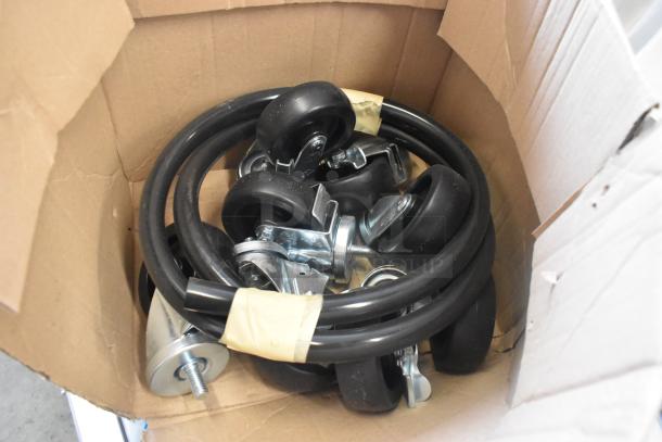 Lot of commercial casters and hoses in a cardboard box, includes several rubber wheels and black tubing, unused condition.