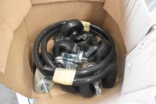 Lot of commercial casters and hoses in a cardboard box, includes several rubber wheels and black tubing, unused condition.