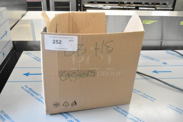 Cardboard box labeled "DB HS Casters" containing commercial casters and hose, auction lot 252, PCI Auctions tag visible.