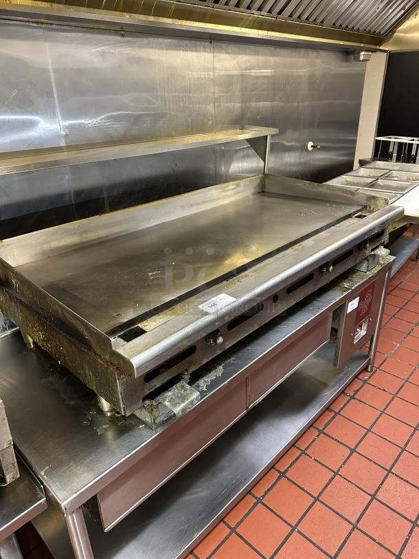 Commercial stainless steel natural gas-powered countertop flat griddle with back and side splash, equipped with legs.