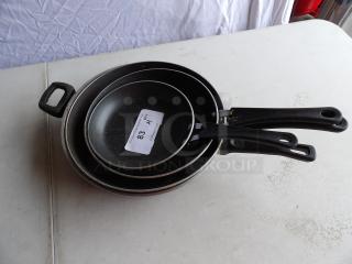 Assorted Traymontina cooking skillets, set of 4, featuring black non-stick surface and ergonomic handles. Visible label "83 QTY."
