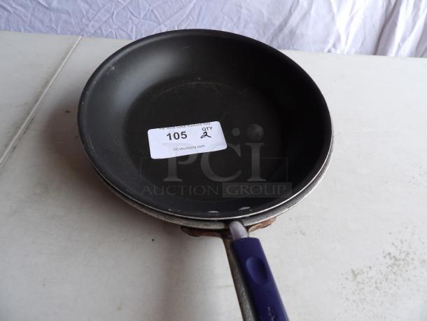 Rachael Ray 12" round aluminum skillet with black non-stick interior and blue handle, auction tag reads "105 QTY 2".