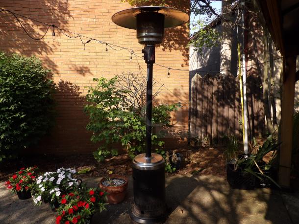 Metal propane gas powered outdoor patio heater in good condition, featuring a tall cylinder design and silver top.