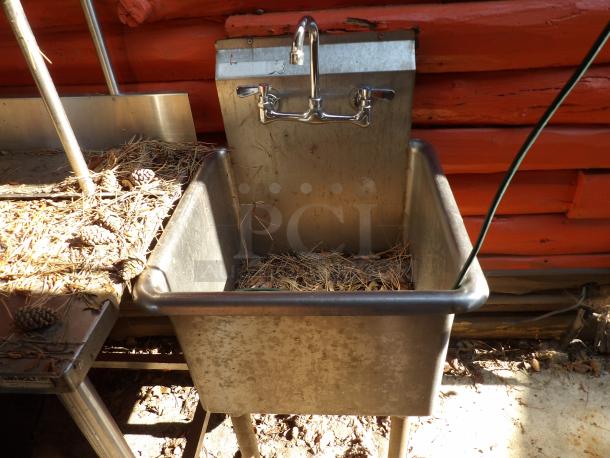 Stainless steel sink with faucet, used condition. Includes backsplash, dual handles, and deep basin. Visible outdoor debris.