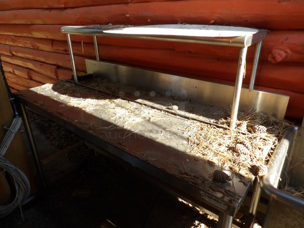 Win-Holt stainless steel table with upper shelf, used condition, featuring metal frame and visible dirt, potential for cleaning.