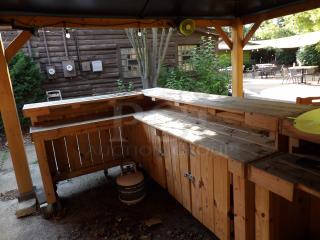 L-Shape wood bar on casters, 8' long, 48" wide, 44" tall. Features natural wood finish, storage cabinets, visible propane tank.
