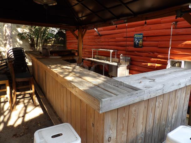 L-Shape wood bar on casters, 8' long, 48" wide, 44" tall, rustic appearance, outdoors, caressed by natural light.