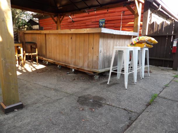 L-shape wood bar on casters, 8' long, 48" wide x 44" tall, in good condition, with additional white stools.
