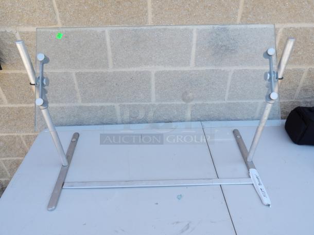 Adjustable height glass food protector on a metal frame. Features include adjustable knobs and asset tag. Good condition.