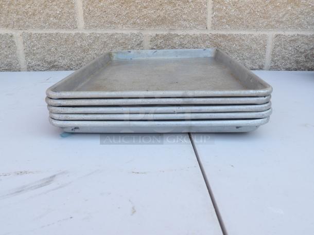 Five half-size sheet pans stacked, showing used condition with some discoloration. Ideal for baking.