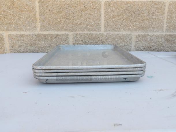 Four stacked half-size aluminum sheet pans, used, with slight discoloration. Durable and ideal for baking.