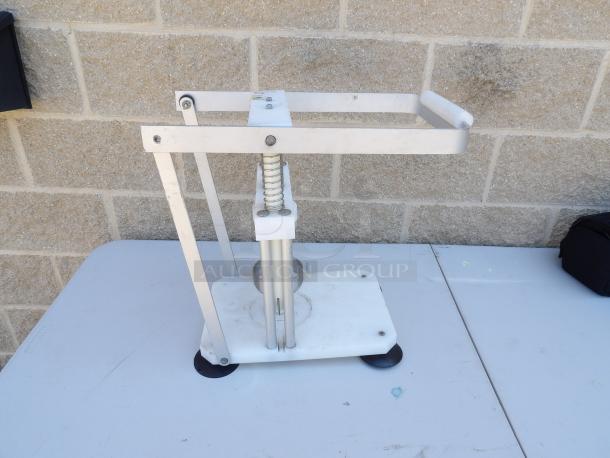 Metal pineapple corer on a white base with a handle and spring mechanism. Appears in good condition with minor wear.