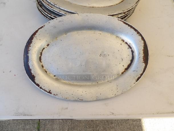11.5" x 8" oval aluminum sizzler platter, weathered with scratch marks and metallic sheen, ideal for serving.