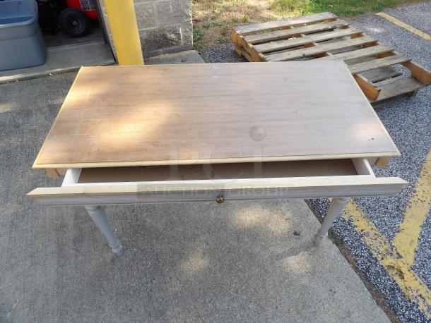 Wood desk with a single open drawer. Features a rectangular top, light finish, and turned legs. Minor surface wear visible.