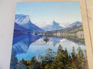 Color photograph of a serene mountain lake with clear blue skies, reflecting rugged peaks and green forest, showcasing natural beauty.
