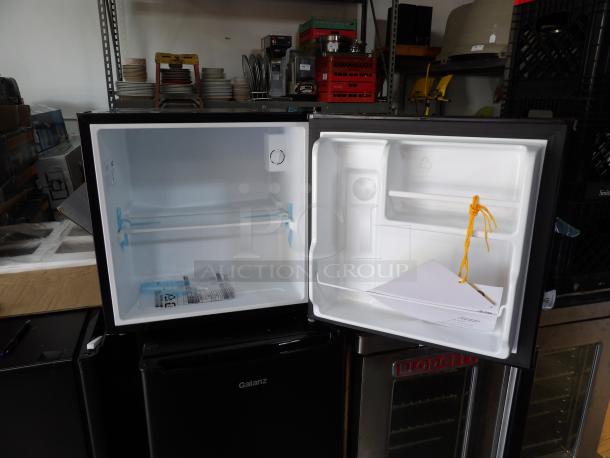 Artic King black single door refrigerator, new, scratch & dent, interior view with shelves and manual inside.