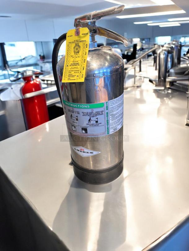AMEREX Model 240 K-Class stainless steel fire extinguisher, top-tier condition, with inspection tag visible.