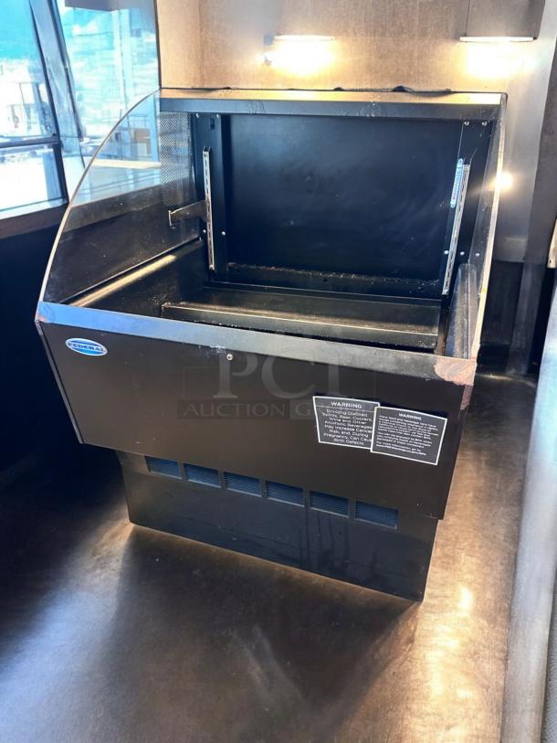 Alt text: Open industrial display case with metal interior and clear top, featuring warning labels on the side.