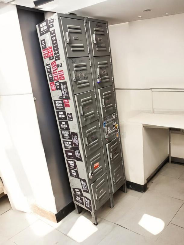 Metal employee locker cabinet with 12 compartments. Good condition, fully functional. Features various stickers and writings.