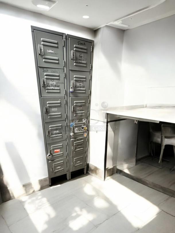 Very good condition metal employee locker cabinet with 12 compartments, featuring visible markings and various stickers. Fully functional.