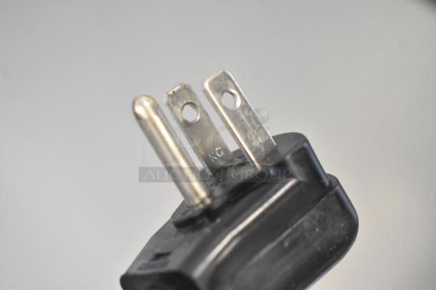 Close-up of a power plug for a Scotsman HID207ABX-1A ice machine, showing metal prongs and part of the black casing.