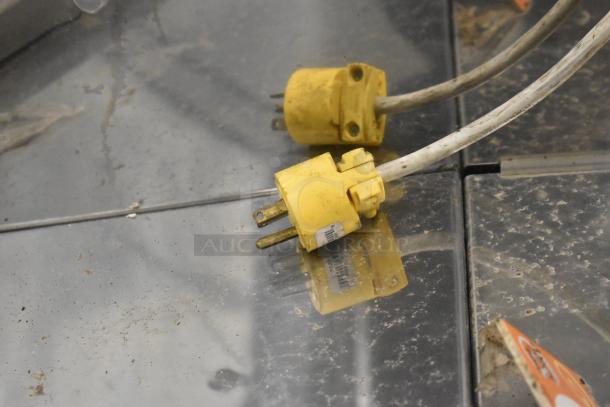 Yellow electrical plugs connected to a Sevel AD-12G Gelato Case Merchandiser, showing some dirt accumulation.