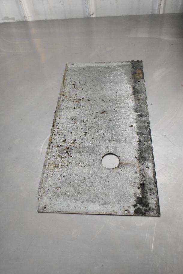 Stainless steel plate with circular cutout, possibly a component of a commercial gas fryer, shows signs of wear and residue.