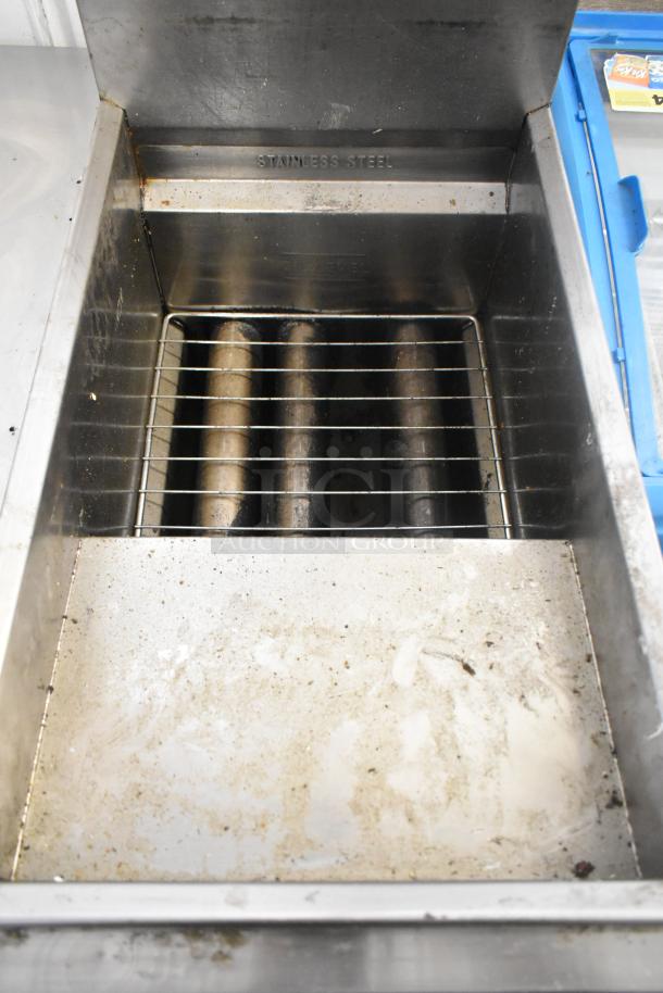 Stainless steel commercial floor-style gas fryer, visible wear, includes wire rack, engraved "Stainless Steel" label.