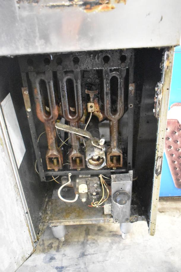 Stainless steel commercial gas-powered deep fat fryer, floor style. Visible wear and internal components shown.