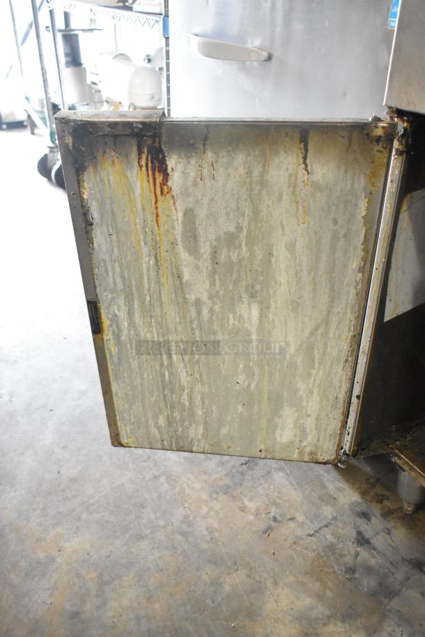 Stainless steel gas-powered commercial deep fat fryer, floor style. Visible wear with grease stains and signs of use.
