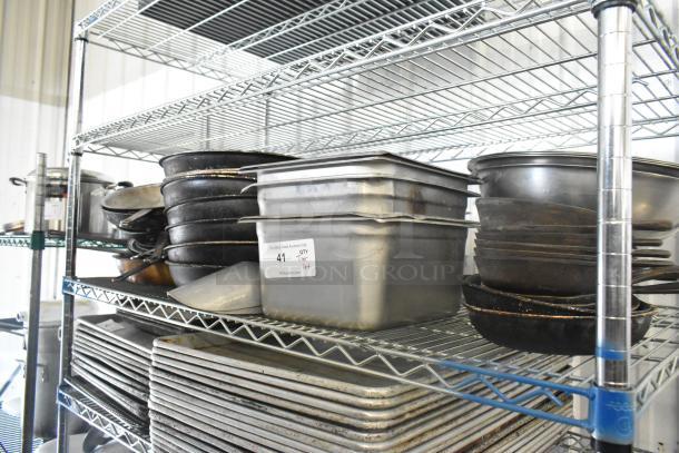Metal shelf with mixed kitchen items: stainless steel drop-in bins, skillets, metal bowls, and baking trays. Auction label visible.