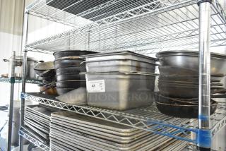 Metal shelf with mixed kitchen items: stainless steel drop-in bins, skillets, metal bowls, and baking trays. Auction label visible.