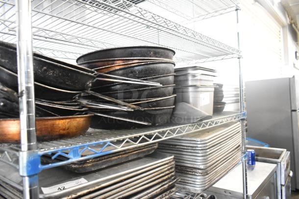 A tiered lot including stainless steel drop-in bins, skillets, and metal bowls stored on wire shelving.