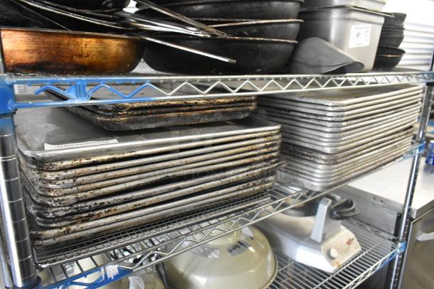 Metal baking pans and various kitchen items on wire shelving, showing signs of wear. Includes stacked pans and kitchen equipment.