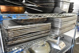 Metal baking pans and various kitchen items on wire shelving, showing signs of wear. Includes stacked pans and kitchen equipment.