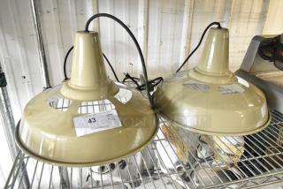 Two beige industrial metal light fixtures with cords, placed on a metal shelf. Tag reads "43, QTY x2."
