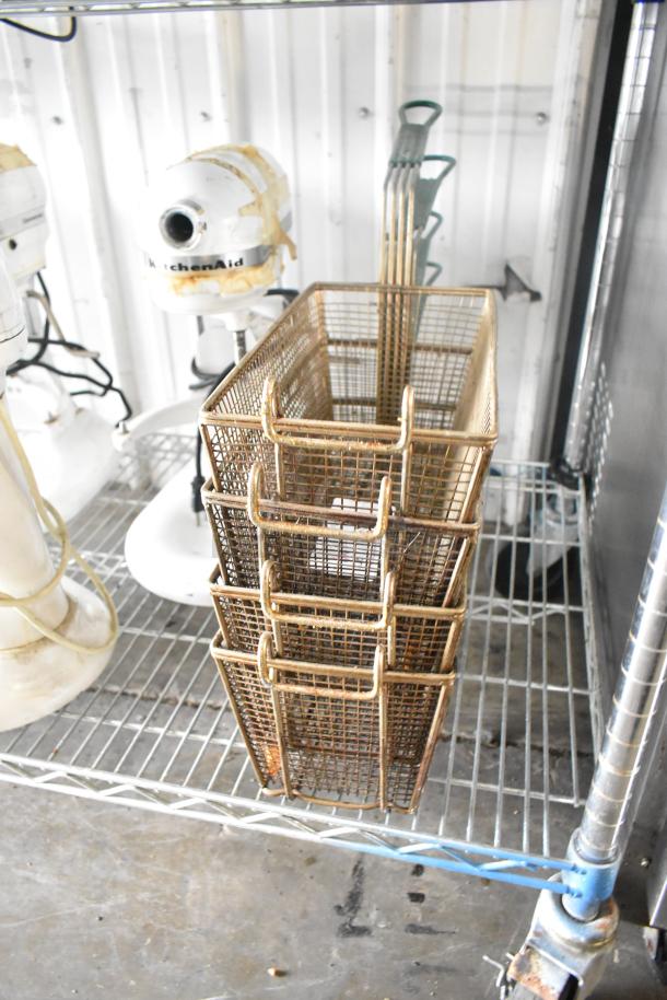 Four metal fry baskets stacked, showing wear, with wire mesh design and handles, ideal for kitchen use.