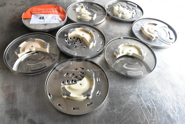 8 KitchenAid metal food processor blades on a scratched surface, showing various designs and cutting styles.