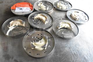 8 KitchenAid metal food processor blades on a scratched surface, showing various designs and cutting styles.