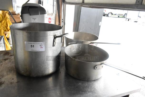 Three metal kitchen items: a large stock pot and two sauce pans with handles. Visible tag reads "51, QTY 3v, PCIAuctions.com."