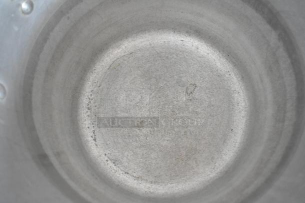 Top view of a metal stock pot interior, showing wear and surface marks, indicating previous use.