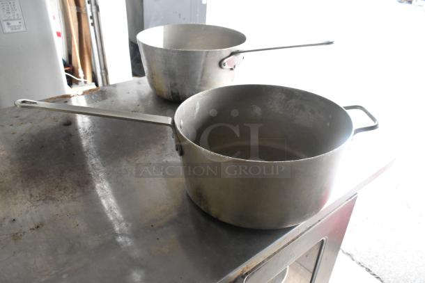 Three metal cookware items including a large stock pot and two saucepans. Visible wear; sturdy design ideal for cooking.