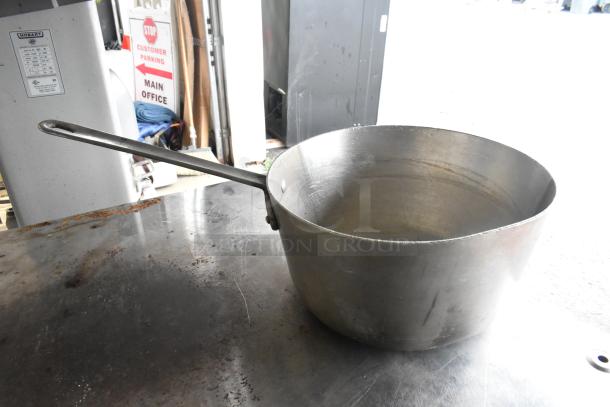 Metal stock pot with long handle, shown on a metallic surface. Moderate wear visible, suitable for durable kitchen use.