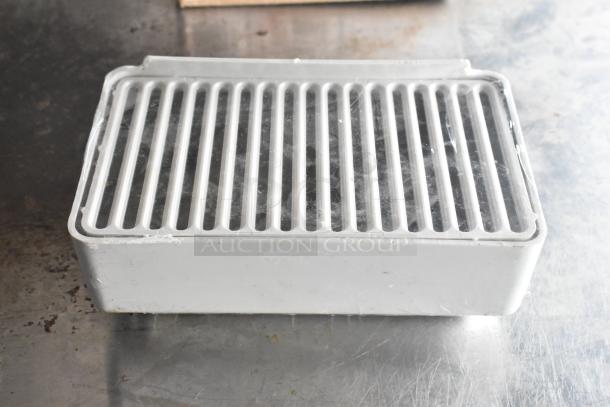 White plastic drip tray on metal surface, featuring a slatted top for drainage. Condition shows signs of use.