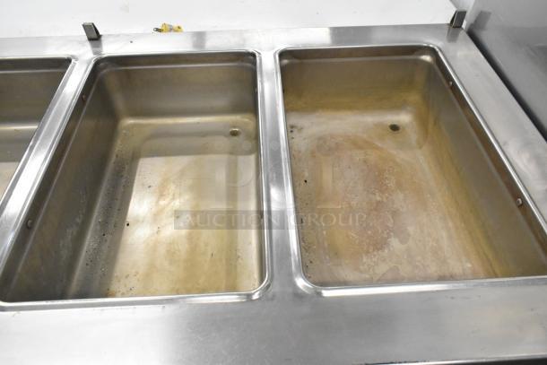 Stainless steel commercial steam table with 4 wells, under shelf, and commercial casters, shows signs of use.