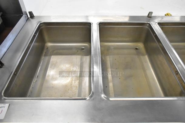 Stainless steel commercial 4-well steam table with under shelf. Features commercial casters, visible signs of light use.