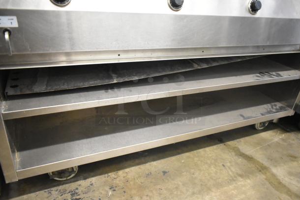 Stainless steel commercial 4 well steam table with under shelf, on commercial casters, showing wear, ideal for catering use.