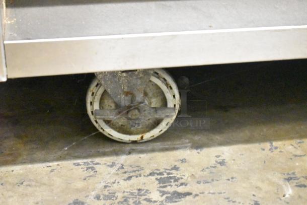 Stainless steel steam table caster wheel, showing dirt and rust; part of 4-well commercial unit with under shelf.