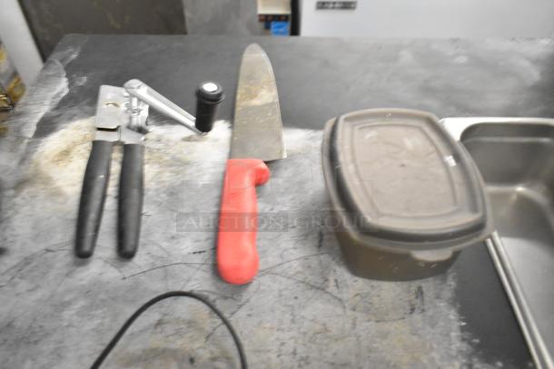 Lot including can opener with black handles, chef knife with red handle, Toastmaster immersion blender base, and a poly bin.