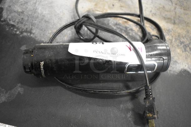 Toastmaster immersion blender base, black, with visible wear. Wire attached. Marked with "PCIAuctions.com" tag.